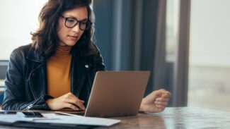 Uma mulher de óculos está trabalhando em seu laptop em uma mesa