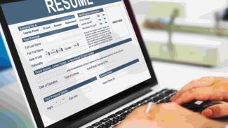 Uma pessoa digitando em um laptop com um currículo