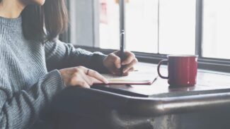 Uma mulher escrevendo em um caderno com uma xícara de café