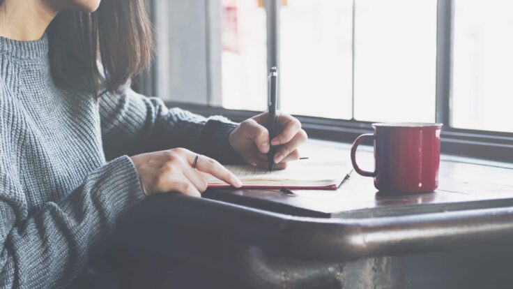 Uma mulher escrevendo em um caderno com uma xícara de café