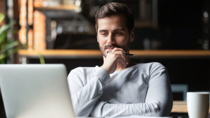 Um homem sentado à mesa com um laptop e uma xícara de café.