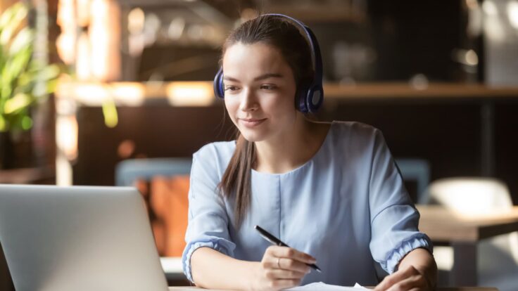 Uma mulher usando um fone de ouvido enquanto trabalhava em um laptop em um café