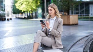 Uma mulher de negócios sentada em uma saliência e usando o celular.