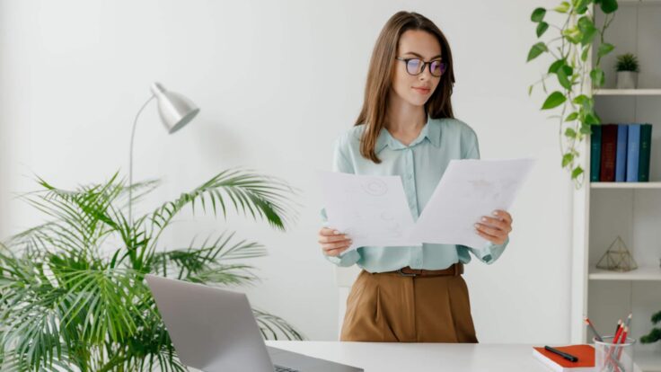 Uma mulher de óculos está diante de uma mesa com papéis à sua frente