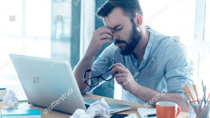 Um homem barbudo sentado em sua mesa com um laptop na mão.