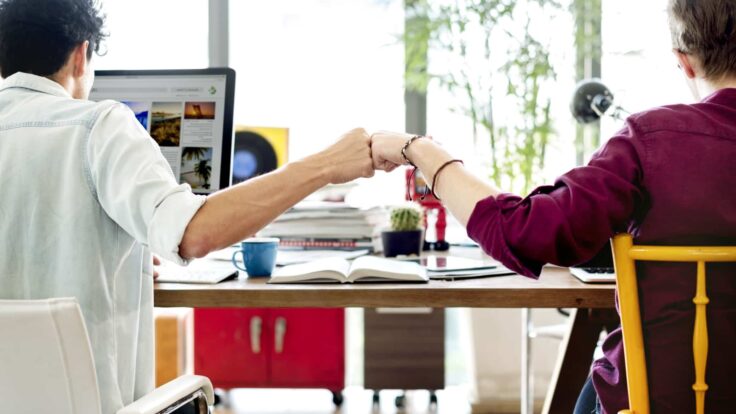Duas pessoas apertando as mãos em uma mesa em frente a um computador.