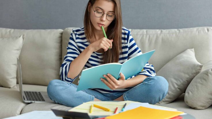 Uma garota sentada em um sofá com um caderno e canetas