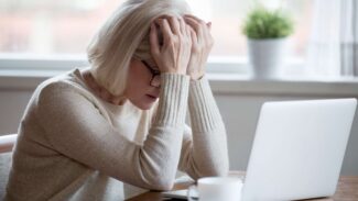 Uma mulher está segurando a cabeça na frente de seu laptop