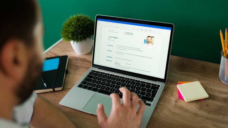 Um homem está usando um laptop com um currículo