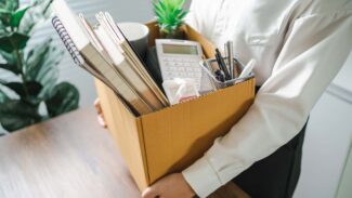 Uma mulher segurando uma caixa de papelão cheia de material de escritório