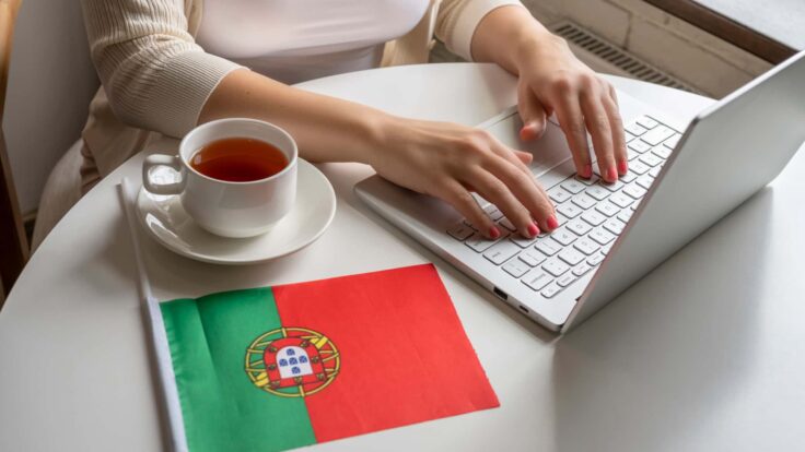 Uma mulher a trabalhar num portátil com uma bandeira portuguesa.