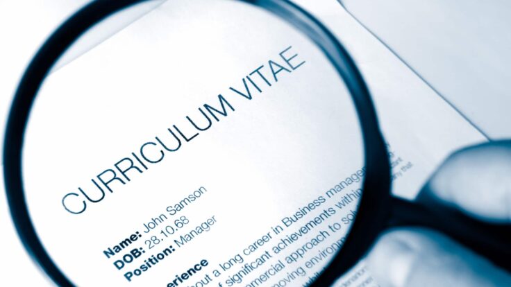 Uma pessoa segurando uma lupa sobre um documento com a palavra curriculum vitae.