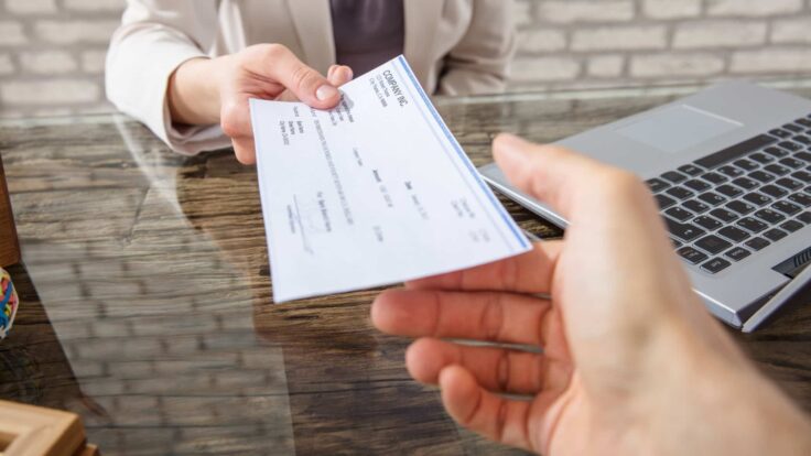 Uma pessoa entregando um cheque a outra pessoa em uma mesa