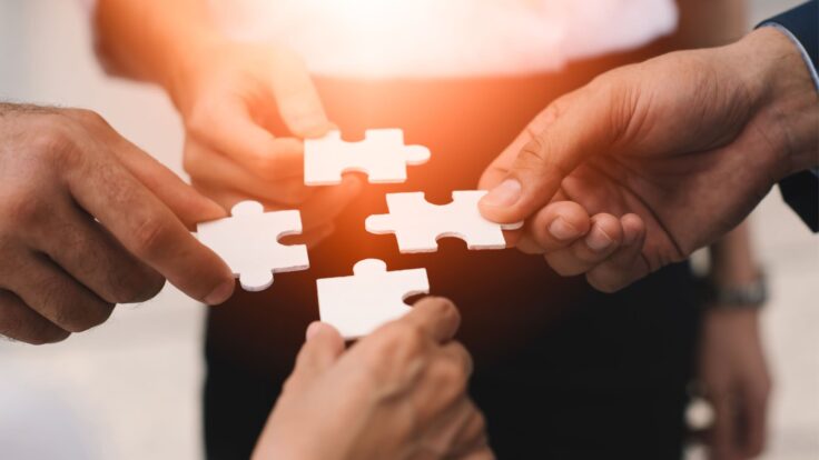Um grupo de empresários segurando uma peça de quebra-cabeça.